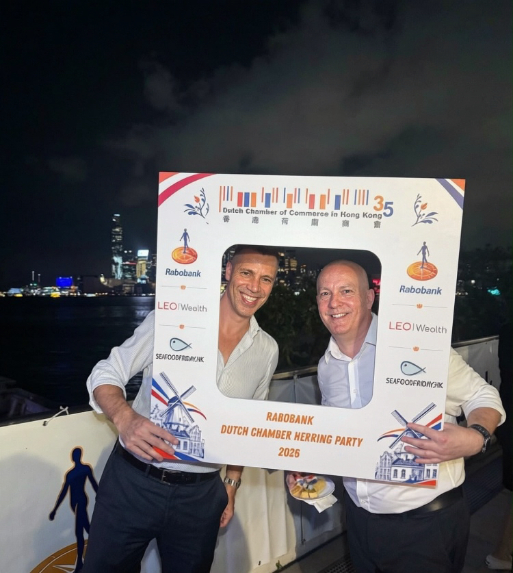 Two guests holding a Dutch Chamber photo frame on a terrace above Victoria Harbour at night